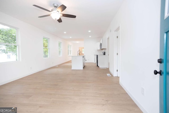 unfurnished living room with baseboards, a sink, light wood-style flooring, and ceiling fan