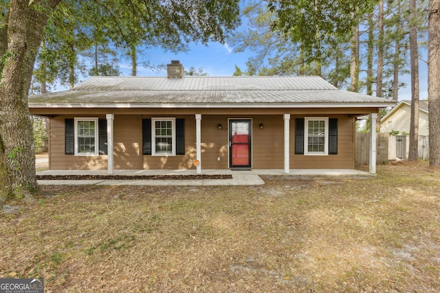 view of front facade featuring fence, a chimney, a porch, and metal roof