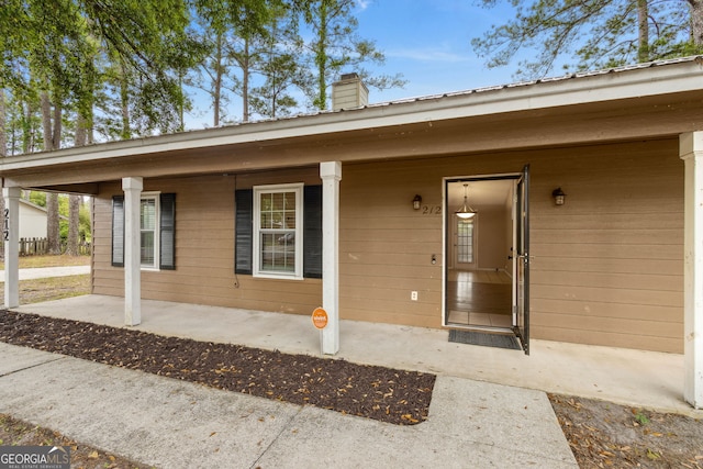 doorway to property featuring a porch, a chimney, and metal roof