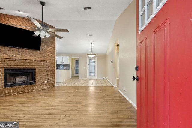 foyer featuring ceiling fan, a brick fireplace, high vaulted ceiling, light wood-type flooring, and visible vents