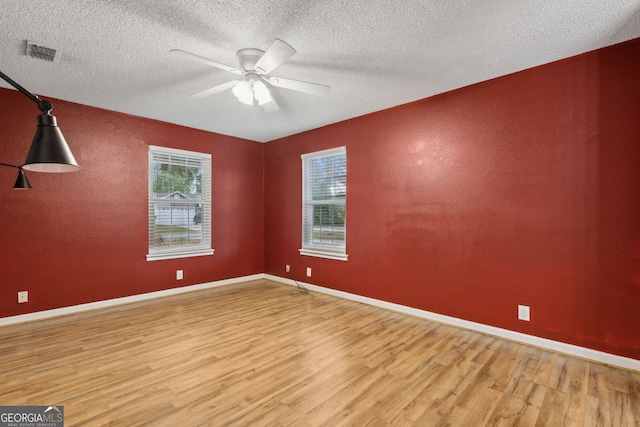 unfurnished room with visible vents, plenty of natural light, wood finished floors, and ceiling fan