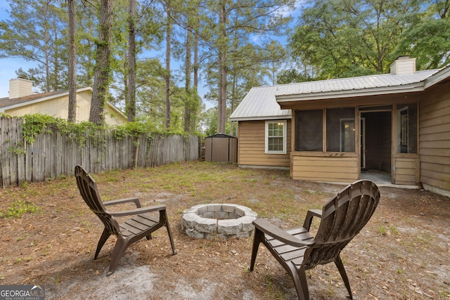 view of yard featuring fence, a storage shed, a sunroom, an outdoor structure, and a fire pit
