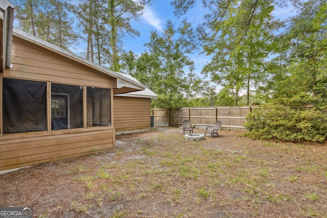 view of yard featuring a fenced backyard, a sunroom, and a fire pit