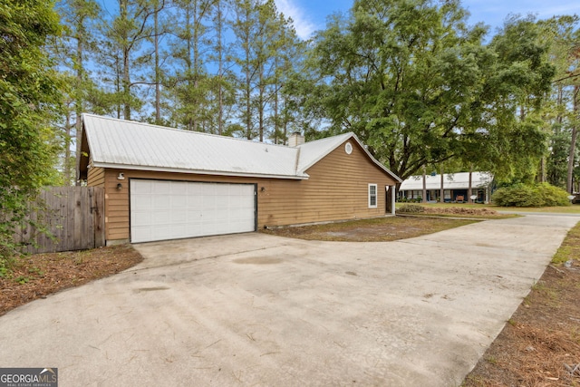 view of side of home with fence, a garage, a chimney, driveway, and metal roof