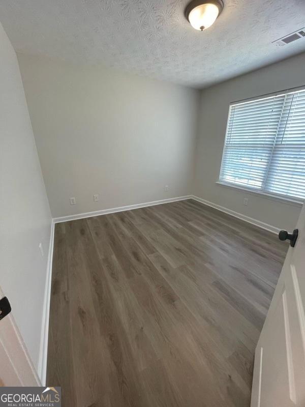 empty room with baseboards, a textured ceiling, visible vents, and wood finished floors