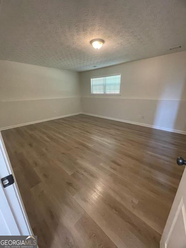 empty room with visible vents, a textured ceiling, baseboards, and wood finished floors