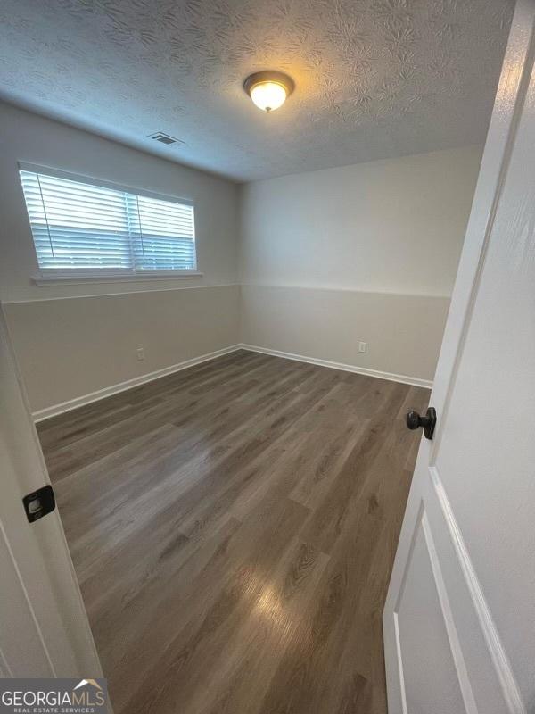 spare room with dark wood-type flooring, a textured ceiling, ceiling fan, and baseboards