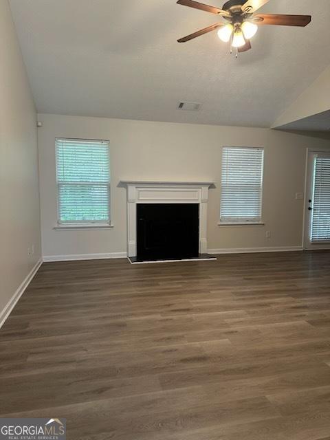 unfurnished living room featuring a fireplace with raised hearth, baseboards, a ceiling fan, and wood finished floors