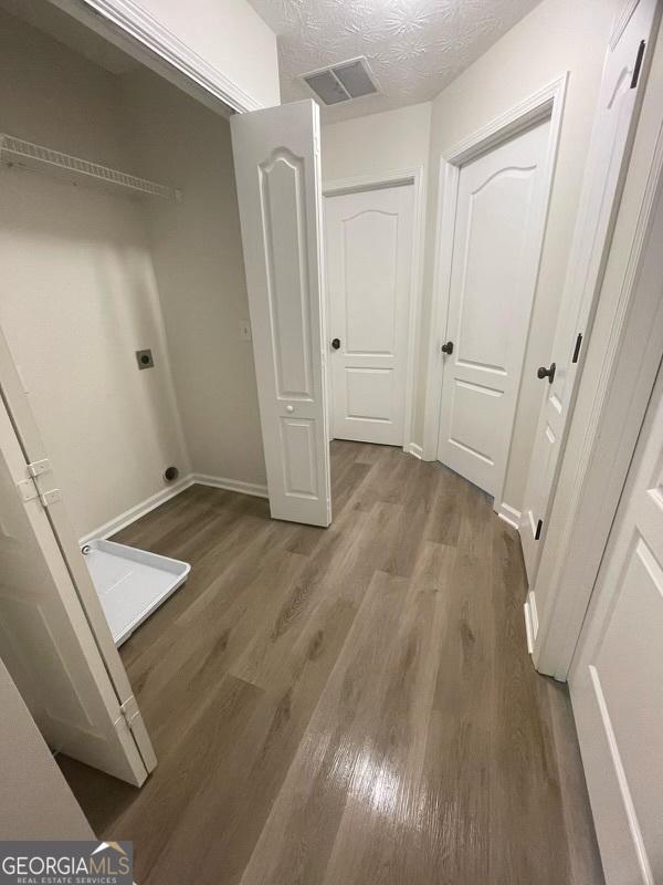empty room with a textured ceiling, baseboards, wood finished floors, and visible vents