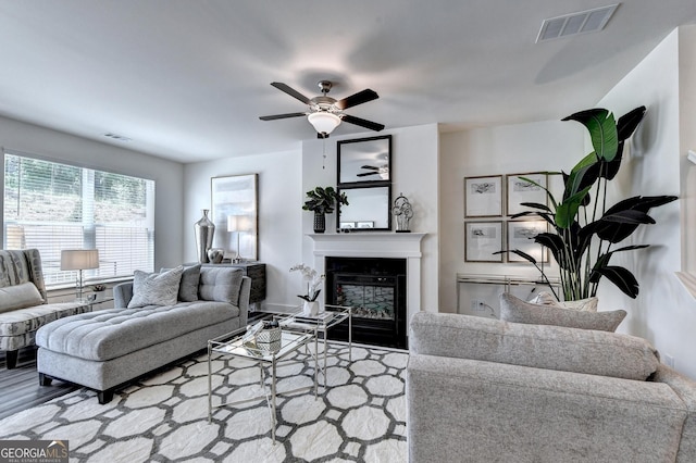 living area with a glass covered fireplace, ceiling fan, wood finished floors, and visible vents