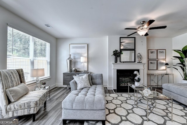 living area with visible vents, a glass covered fireplace, wood finished floors, baseboards, and a ceiling fan