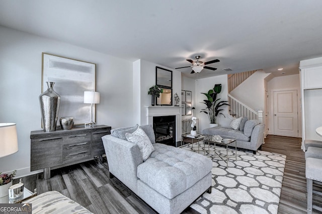 living room with a ceiling fan, a glass covered fireplace, stairway, and dark wood-type flooring