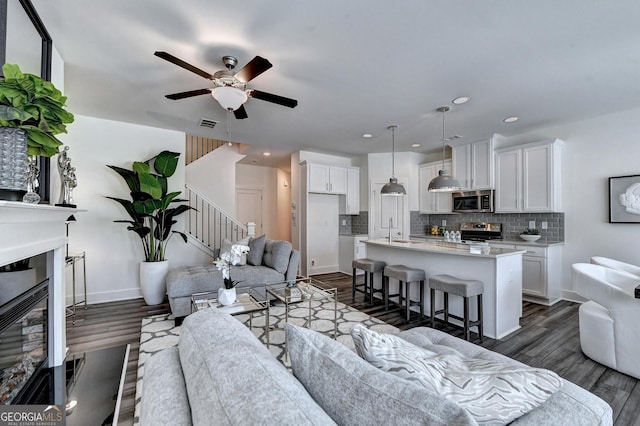 living area with a glass covered fireplace, ceiling fan, dark wood-style floors, stairway, and recessed lighting