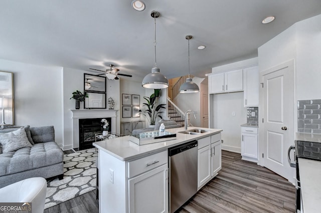 kitchen featuring dishwasher, a sink, white cabinets, open floor plan, and a glass covered fireplace