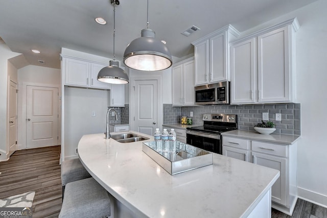 kitchen featuring a sink, stainless steel appliances, baseboards, visible vents, and a center island with sink