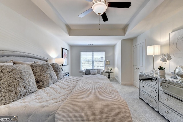bedroom featuring light colored carpet, a ceiling fan, and a tray ceiling