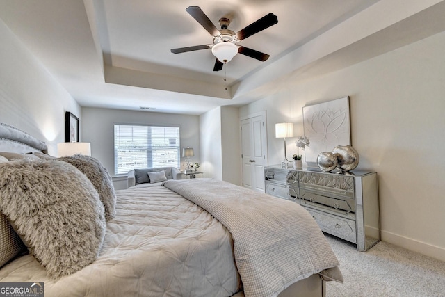 bedroom with ceiling fan, a tray ceiling, light colored carpet, and baseboards
