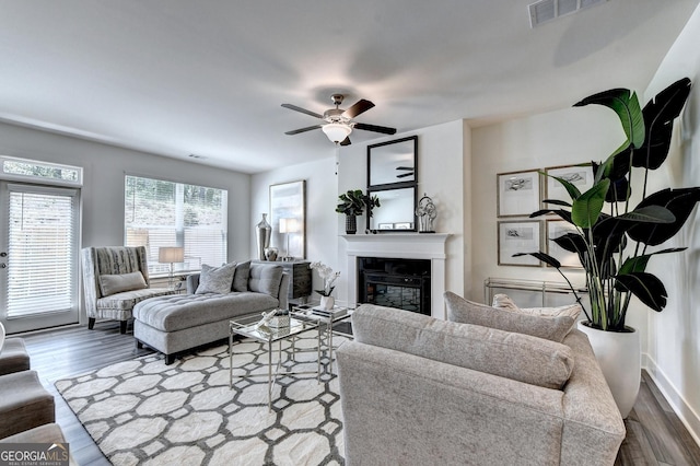 living area with a glass covered fireplace, ceiling fan, dark wood finished floors, and visible vents
