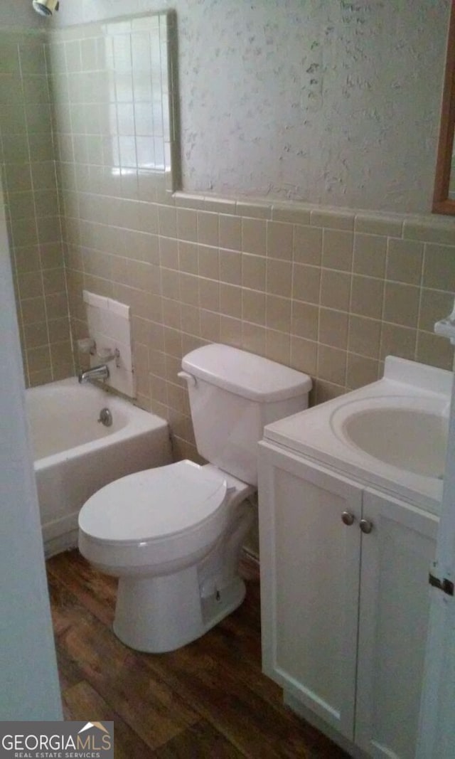 bathroom featuring vanity, toilet, tile walls, bathing tub / shower combination, and wood finished floors