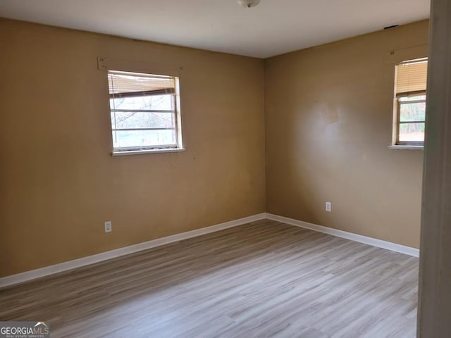 spare room featuring baseboards, wood finished floors, and a wealth of natural light