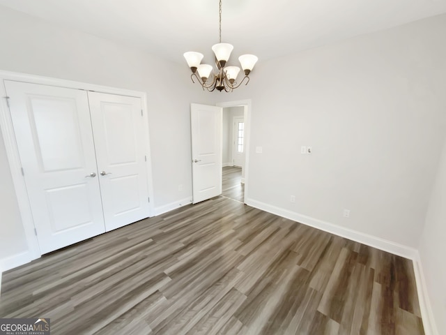 unfurnished dining area with baseboards, wood finished floors, and a notable chandelier