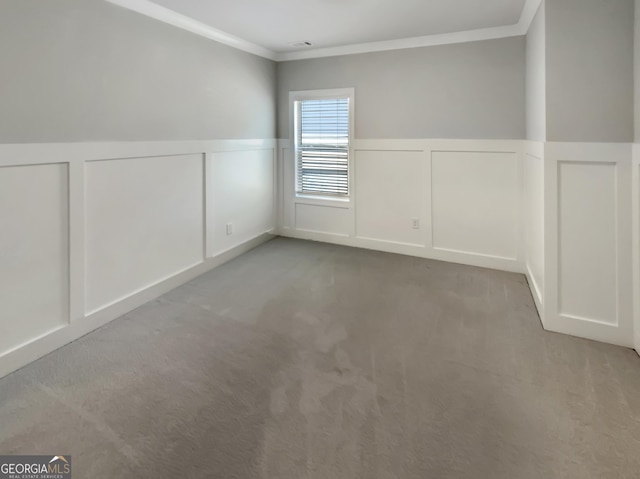 carpeted empty room featuring crown molding, wainscoting, and a decorative wall