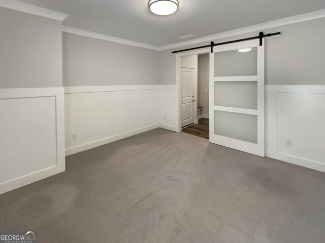 unfurnished bedroom featuring crown molding, carpet floors, a decorative wall, a barn door, and a wainscoted wall