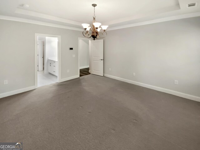 unfurnished room with a notable chandelier, dark carpet, baseboards, a tray ceiling, and visible vents