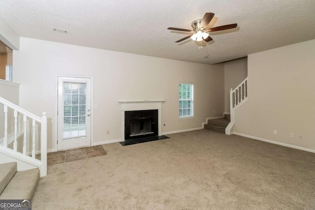 unfurnished living room featuring visible vents, ceiling fan, stairway, a textured ceiling, and carpet flooring