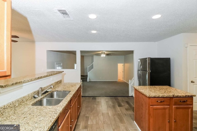 kitchen with brown cabinetry, a textured ceiling, wood finished floors, a sink, and freestanding refrigerator