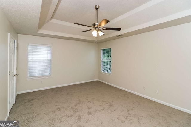 carpeted empty room featuring ceiling fan, a textured ceiling, visible vents, baseboards, and a tray ceiling