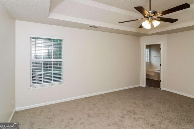 carpeted spare room with a textured ceiling, a ceiling fan, baseboards, a tray ceiling, and visible vents