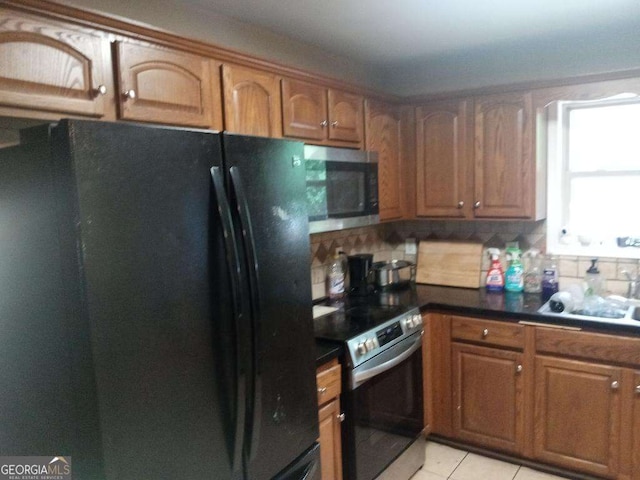 143 Delane Dr, Dallas, GA 30157 - kitchen with dark countertops, light tile patterned floors, brown cabinets, appliances with stainless steel finishes, and backsplash