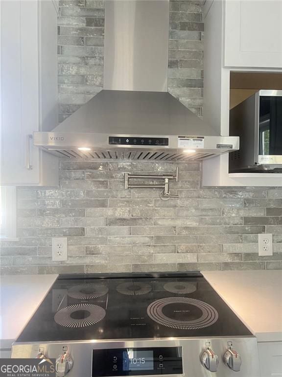 kitchen with wall chimney range hood, white cabinets, stove, and light countertops