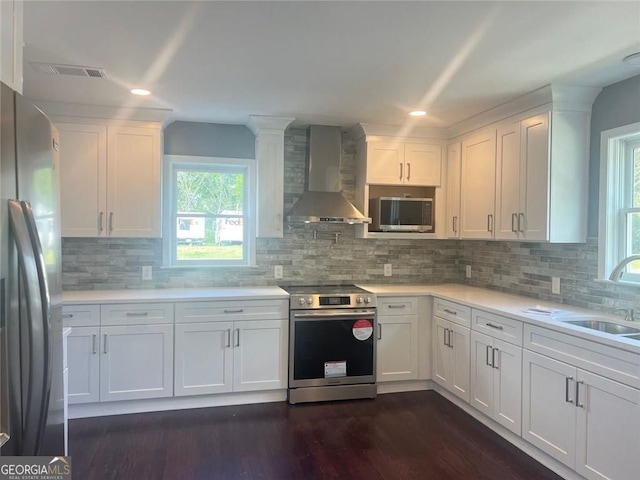kitchen featuring wall chimney exhaust hood, appliances with stainless steel finishes, a sink, white cabinetry, and light countertops