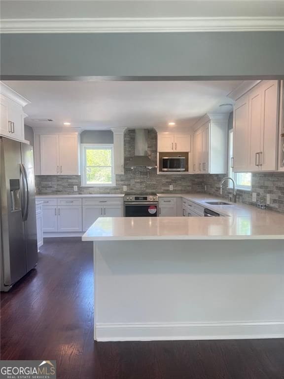 kitchen with stainless steel appliances, wall chimney range hood, a sink, light countertops, and a peninsula