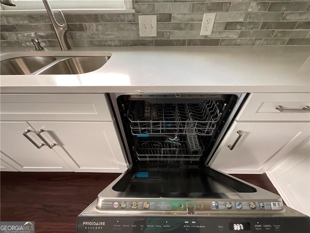 kitchen view of a sink, white cabinetry, dishwasher, and backsplash