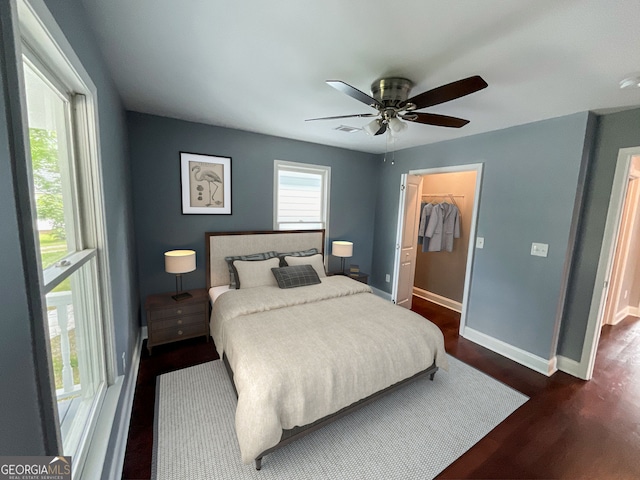 bedroom with baseboards, dark wood-style flooring, a spacious closet, and ceiling fan