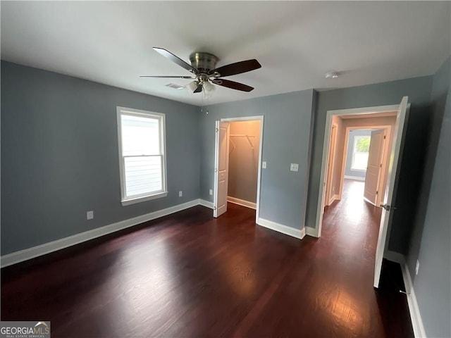 unfurnished bedroom featuring dark wood-style flooring, multiple windows, baseboards, and a ceiling fan