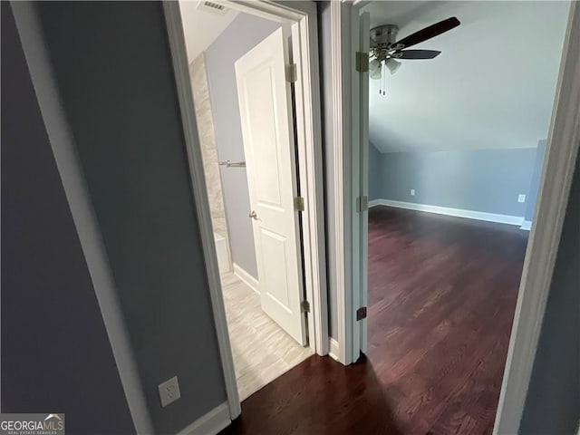 hallway with wood finished floors, lofted ceiling, and baseboards