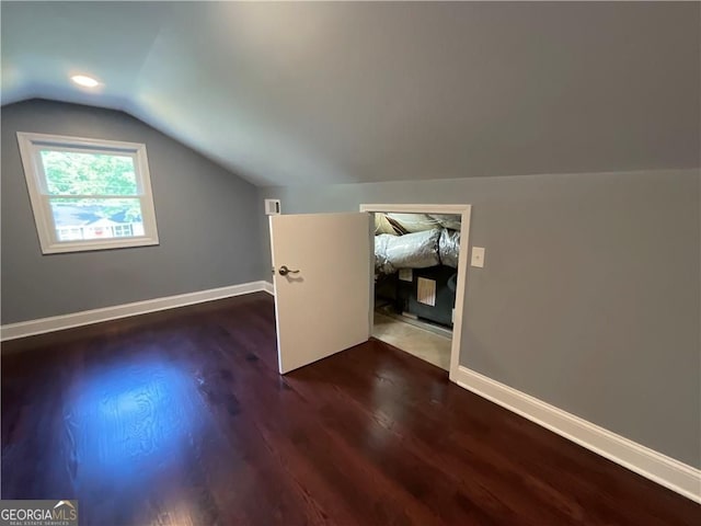 additional living space featuring dark wood-style floors, vaulted ceiling, and baseboards