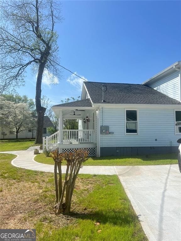 view of side of home with a porch, roof with shingles, a yard, and crawl space
