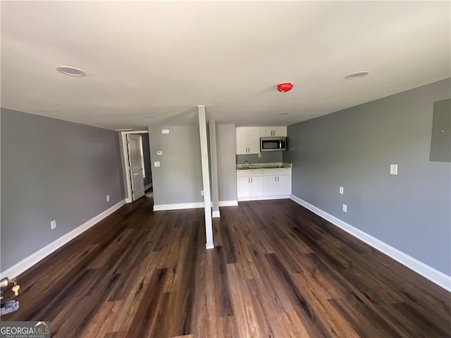 unfurnished living room featuring baseboards, dark wood-style floors, and electric panel