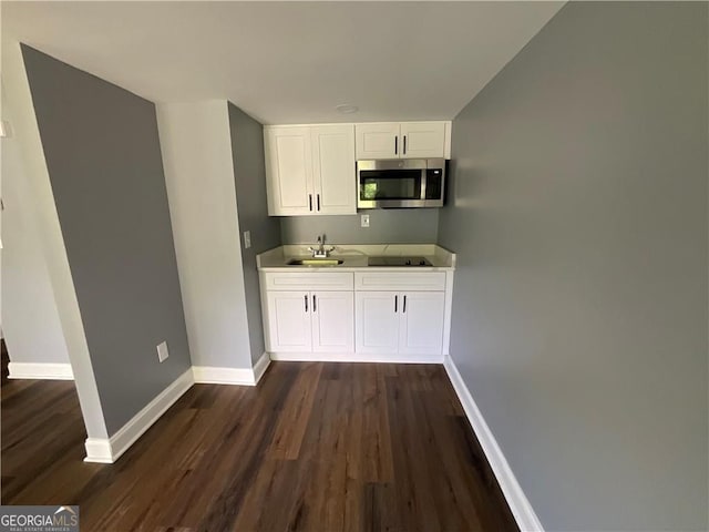kitchen with stainless steel microwave, dark wood-style floors, white cabinetry, black electric cooktop, and baseboards