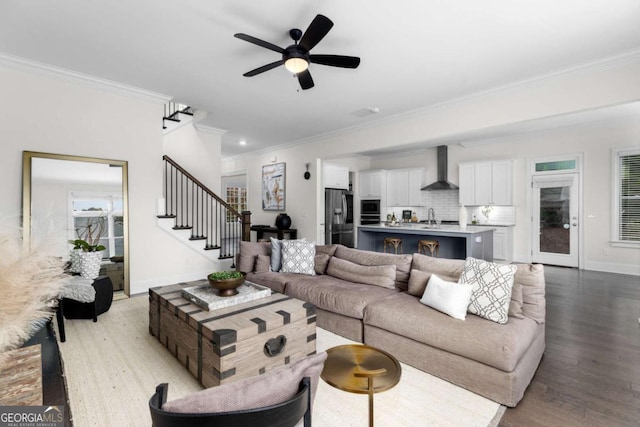 living area featuring a ceiling fan, crown molding, wood finished floors, baseboards, and stairs
