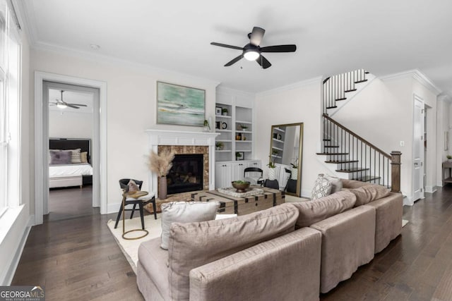 living area featuring crown molding, a ceiling fan, a glass covered fireplace, and dark wood-type flooring