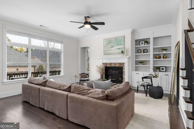 living room with a glass covered fireplace, dark wood finished floors, a ceiling fan, visible vents, and ornamental molding