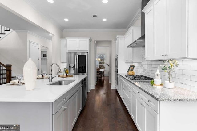 kitchen with wall chimney range hood, white cabinets, a sink, stainless steel appliances, and visible vents