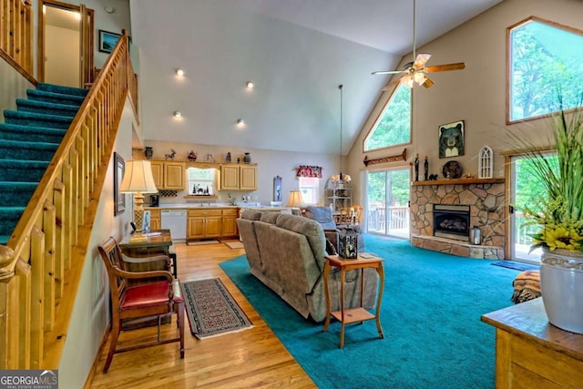 living room with a stone fireplace, high vaulted ceiling, stairway, light wood-type flooring, and a ceiling fan