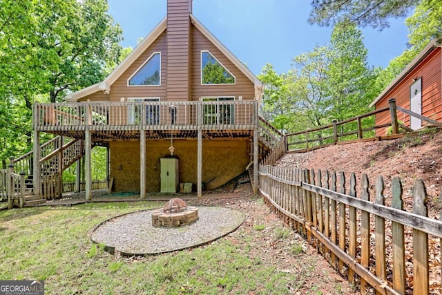 back of property featuring a chimney, a wooden deck, stairway, a fenced backyard, and a fire pit